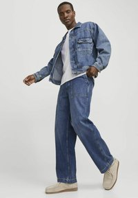 Chaqueta de mezclilla y jeans en azul intermedio, con un diseño relajado, dos bolsillos frontales y un collar clásico. Zapatos beige completan el atuendo.