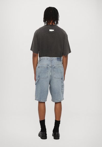 Back view of a person wearing a dark gray t-shirt and light blue denim cargo shorts with pockets and rolled hems, paired with black socks and shoes.