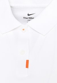 Polo blanc Nike avec col pointu, deux boutons et une petite étiquette en tissu orange sur la patte de boutonnage.