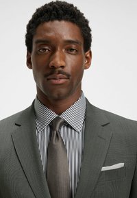 Dark gray suit with a textured weave, paired with a black and white striped shirt. Dark satin tie and white pocket square complete the look.