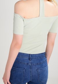 Ljusgrön avskuren topp med korta ärmar, matchad med högmidjade blå denimjeans med två bakfickor och en slät textur.