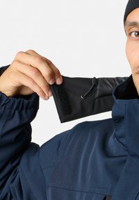 Navy jacket with elastic cuffs and black details, featuring a velcro strap and a drawstring for adjustment. Smooth texture and casual design.