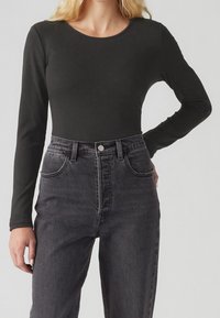 Svart ribbat långärmad topp i kombination med högmidjade mörka jeans i denim som har en knappstängning framtill och två sidofickor.