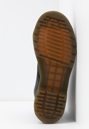 Sole of a black leather boot with translucent brown rubber tread, positioned upright against white walls and floor.