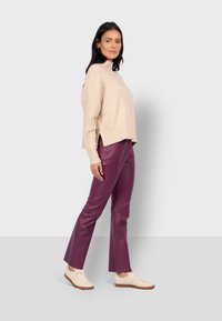 Suéter beige de canalé, corto con aberturas laterales, combinado con pantalones de cuero morados ajustados y zapatillas crema. Diseño de atuendo simple y moderno.