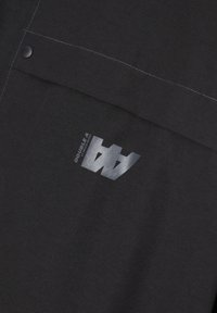 Black fabric with contrasting white stitching. Features a printed logo in metallic silver. Design includes snap button details.