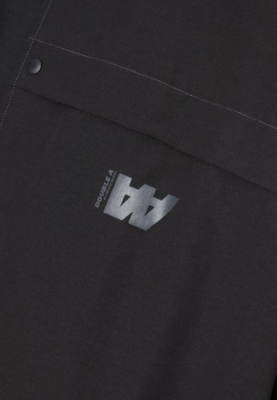 Schwarzer Stoff mit kontrastierenden weißen Nähten. Verfügt über ein gedrucktes Logo in metallic Silber. Das Design beinhaltet Druckknopf-Details.