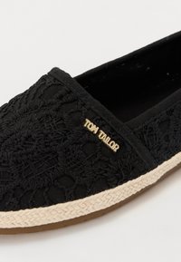 Crne slip-on cipele s teksturiranim čipkastim premazom, s zlatnim logotipom "Tom Tailor" i pletenim jutenim obrubom oko đona.