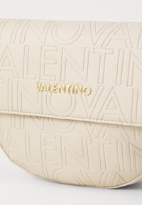 Beige skinnveske med preget "VALENTINO"-logo, med gullfargede detaljer og teksturert overflate for en matt finish.