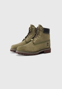 Botines de ante verde con suela de goma marrón, ojales dorados, cordones marrones, cuello acolchado y detalle del logo de Timberland en el costado.
