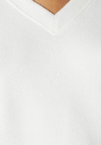 Maglione bianco a V realizzato in un morbido tessuto testurizzato. Il colletto ha un design pulito e semplice, che enfatizza il suo minimalismo.