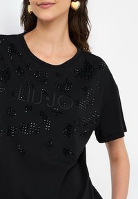 T-shirt nera a maniche corte con decorazioni nere lucide e il testo "LIU JO" in finitura opaca sul davanti, girocollo.