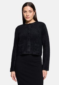 Czarny krótkowłosy kardigan o miękkiej, puszystej fakturze; okrągły dekolt; zapięcie na guziki z przodu; dwie przednie kieszenie; długie rękawy.