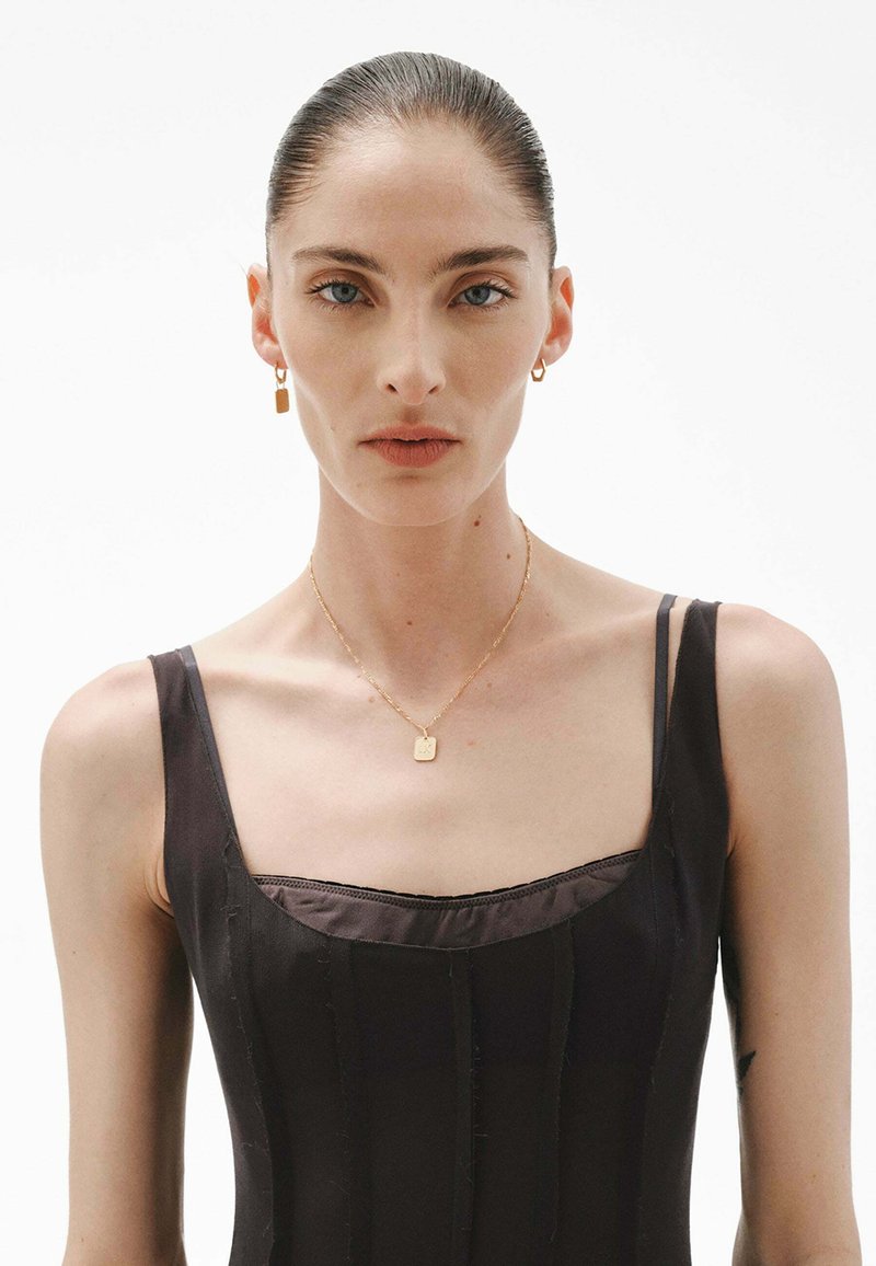 Vestido negro sin mangas con escote cuadrado, collar de cadena dorada con un colgante rectangular y aros dorados a juego.