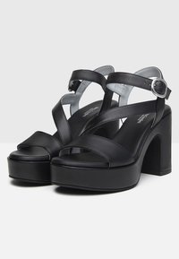 Sandali platform neri con finitura in pelle liscia, dotati di fasce incrociate e chiusura a fibbia. Design con tacco spesso e punta aperta.