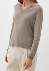 Pull beige en maille avec un col en V, coupe slim, et poignets et ourlet côtelés. Associé à un pantalon large texturé de couleur claire.