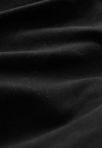 Black fabric with a fine ribbed texture, showing soft folds and slight sheen, emphasizing depth and movement in the material.