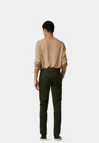 Kaki Langarmhemd, weicher Stoff, Rundhalsausschnitt. Grüne Slim-Fit-Hose, glatte Textur, kontrastierender gemusterter Gürtel, schwarze Schuhe. Rückansicht.