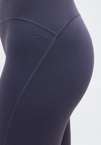 Κοντινό πλάνο μαύρο καλσόν αθλητικού τύπου με ραμμένα ραφές και ανάγλυφο λογότυπο «BORG» στο πάνω μέρος του μηρού.