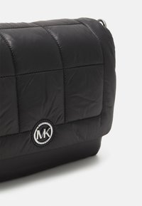 Borsa a tracolla nera trapuntata con logo rotondo in argento e superficie liscia. Presenta una forma rettangolare e una costruzione in tessuto resistente.