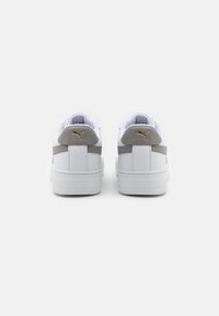 Vita sneakers med en texturerad grå accent och guld-logotyp på hälen. Enkelt design, låg toppsilhuett med en slät yta.