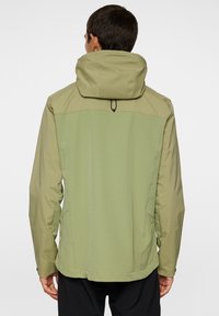 Vandtæt jakke i lys olivengrøn, med høj krave, justerbar hætte og sidelommer. Glat tekstur og minimalistisk design.
