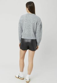 Pull gris tricoté avec ourlet et poignets côtelés, associé à un short en simili cuir noir. Le mannequin porte des baskets blanches avec des chaussettes texturées.