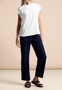 Top bianco a maniche corte, jeans ampi blu scuro e sandali marroni con motivo. Design semplice e casual con linee pulite e una vestibilità rilassata.