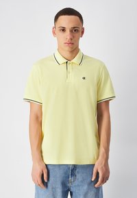 Jasnożółta koszulka polo z klasycznym kołnierzykiem, czarnymi akcentami na kołnierzyku i mankietach oraz małym logo na lewej piersi.