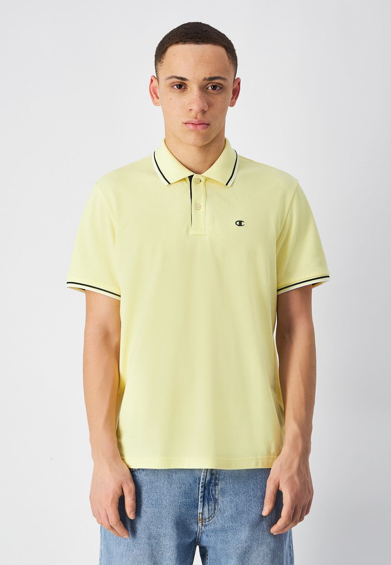 Jasnożółta koszulka polo z klasycznym kołnierzykiem, czarnymi akcentami na kołnierzyku i mankietach oraz małym logo na lewej piersi.