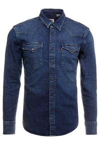Chemise en denim bleu foncé à manches longues avec fermeture par boutons, deux poches poitrine à rabat boutonné et col classique.
