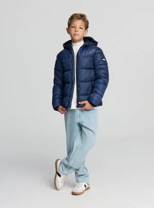 Granatowa pikowana kurtka z zamkiem błyskawicznym i kapturem, o gładkiej fakturze. Połączona z jasnymi dżinsami i białymi tenisówkami.