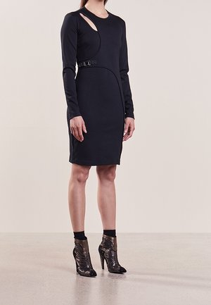 Robe noire à manches longues avec un détail découpé, des coutures courbes et une accentuation par boucle à la taille ; associée à des bottes à talons haut texturées.