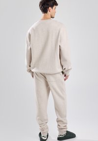 Felpa in pile beige e pantaloni jogger, vestibilità rilassata con polsini a coste. I pantaloni presentano una tasca laterale, abbinati a scarpe slip-on verdi.