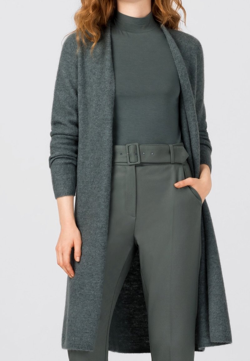 Dlouhý kardigan s otevřeným předním dílem v měkké šedozelené pletenině, zkombinovaný s odpovídajícím rolákem a kalhotami s vysokým pasem a přizpůsobeným střihem s páskem.