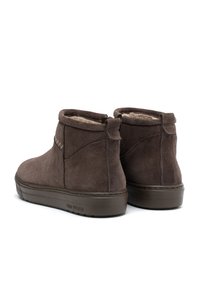 Botas de tobillo de ante marrón con un forro suave, que presentan un tacón bajo y redondeado y un diseño sencillo. Incluyen un tirador en la parte posterior para facilitar su uso.