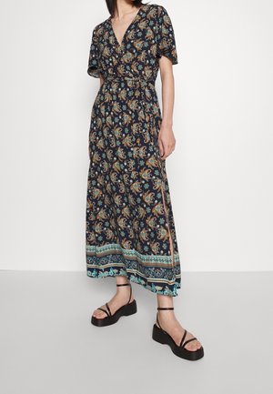 Lungo vestito scuro a fiori con scollo a V, maniche corte e vita cintrata. Presenta motivi paisley blu e arancioni e spacchi laterali. Indossato con sandali neri.