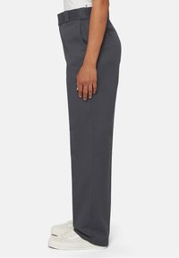 Pantalons gris à jambes droites avec une texture lisse, dotés d'une taille standard et de poches latérales, associés à des baskets blanches.