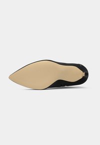 Zapato de tacón alto negro con punta afilada, que presenta una suela de goma beige. Material superior liso sin patrones visibles ni herrajes.