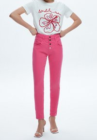 Rosa högmidjade jeans med fem knappar, två framfickor och smal passform, matchade med en vit t-shirt med ett rödblommigt konturdekor.