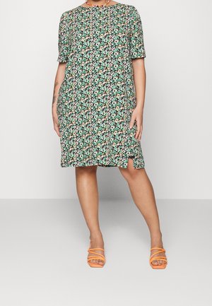 Schwarzes Blumenkleid mit grünen, rosa und gelben Mustern, kurzen Ärmeln, lockerer Passform, seitlichen Schlitzen und orangefarbenen Riemchensandalen.