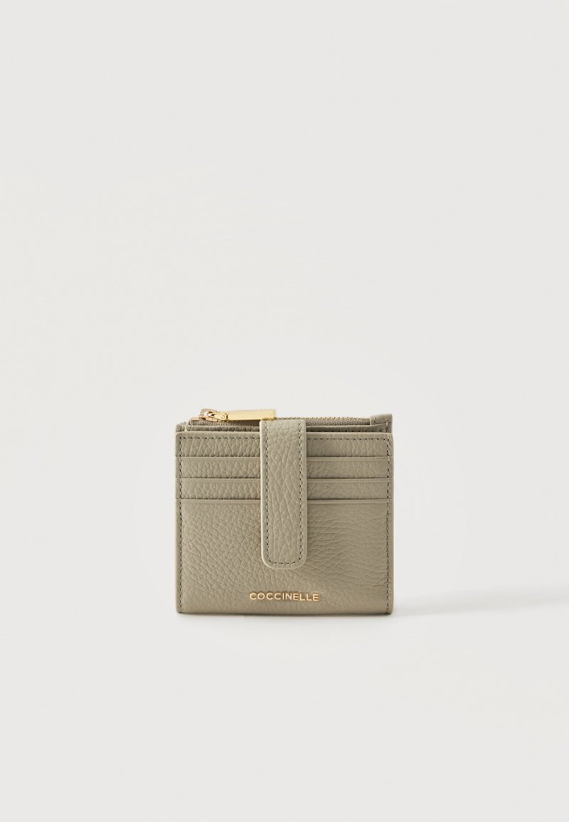 Petit portefeuille en cuir vert olive avec plusieurs emplacements pour cartes, une sangle à fermeture pression et un compartiment supérieur zippé, marqué « Coccinelle » en lettres dorées.