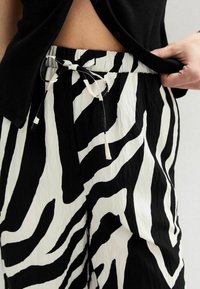 Pantalons à motif zèbre noir et blanc avec taille à cordon, fabriqués en tissu léger présentant une texture froissée.