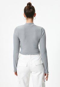 Haut à manches longues gris à côtes avec un ourlet court, un col rond et un tissu texturé. Porté avec un pantalon blanc comportant des poches cargo.