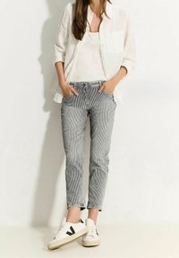 Chemise blanche à boutons portée sur un débardeur blanc, associée à un pantalon rayé noir et blanc et des baskets blanches avec des accents noirs.