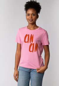 Roze katoenen t-shirt met opvallende rode "CINCIN" tekst. Korte mouwen, ronde hals en een losse pasvorm. Zachte textuur. Gecombineerd met blauwe spijkerbroek.