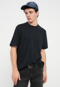 Μαύρο βαμβακερό κοντομάνικο μπλουζάκι με κλασικό στρογγυλό λαιμό, συνδυασμένο με σκούρα τζιν και υφασμένο μπλε καπέλο.