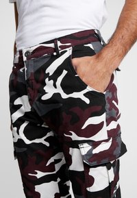 Camo cargo pants with maroon, black, gray, and white colors. Features side pocket, button closure, and sturdy fabric for durability.