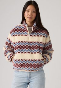 Φλις πουλόβερ σε κρέμ χρώμα με κόκκινα και μπλε ζιγκ-ζαγκ σχέδια, με γιακά με φερμουάρ μέχρι τη μέση και πλαϊνές τσέπες. Μαλακή υφή, χαλαρή εφαρμογή.