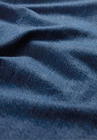 Tummansinisestä denim-kankaisesta materiaalista, jossa on pehmeä, teksturoitu pinta ja näkyviä poimuja ja ryppyjä, jotka korostavat sen kolmiulotteista ulkonäköä.